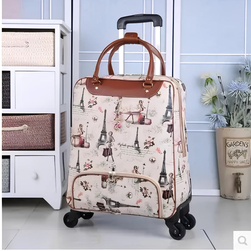 A soft-sided rolling suitcase with a Paris-themed print featuring Eiffel Towers, vintage women, and script text. The suitcase has a cream-colored background, brown leather handles and trim, and four black spinner wheels.
